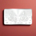 Load image into Gallery viewer, A rectangular 999 purity silver coin with two figures, Ganeshji and Lakshmiji, seated on a lotus design with floral patterns around it.