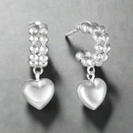 Load image into Gallery viewer, A pair of sterling silver hoop earrings with heart-shaped embellishments and pearl-like beads.