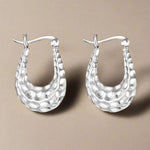 Load image into Gallery viewer, A pair of silver hoop earrings with a hand textured design, displayed against a white background.