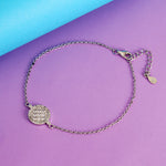 Load image into Gallery viewer, Silver bracelet with a round, diamond-studded charm on a purple and blue background
