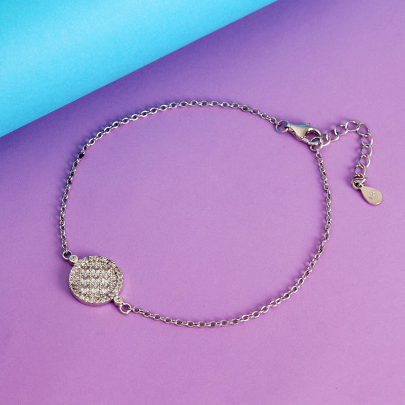Silver bracelet with a round, diamond-studded charm on a purple and blue background