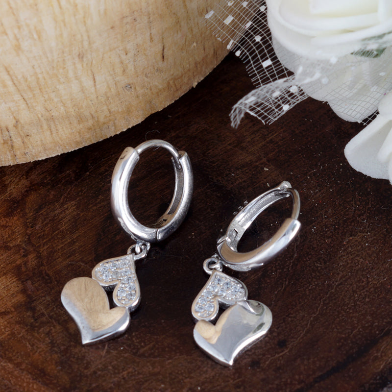 Silver heart-shaped earrings on a wooden surface with white flowers.