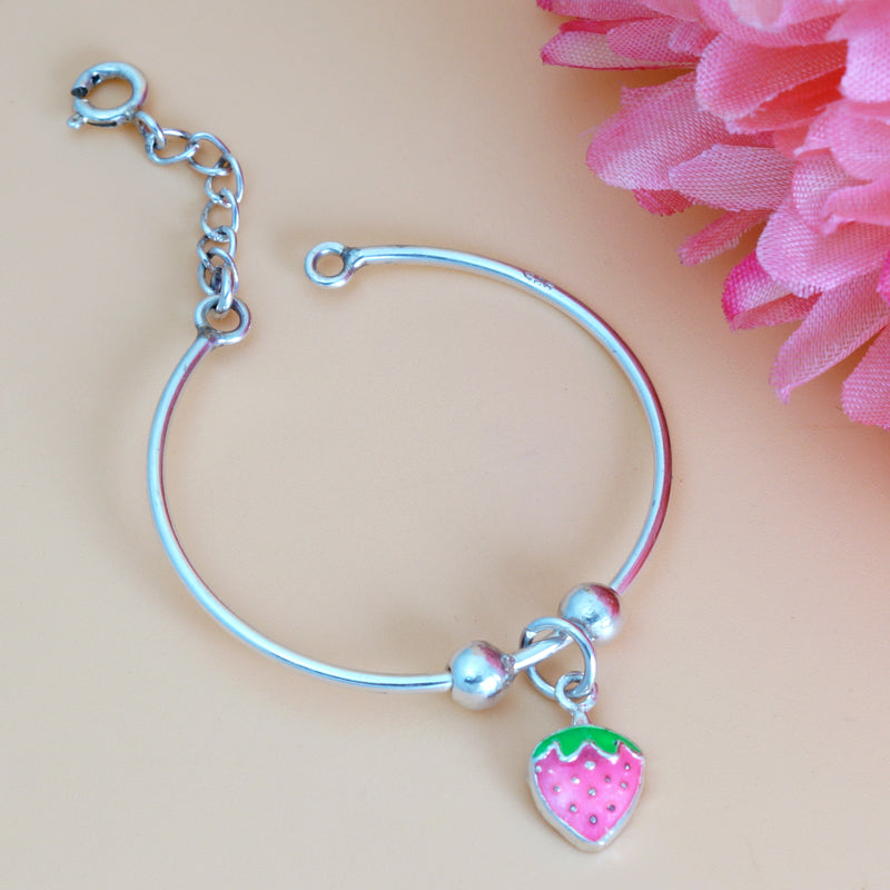 Silver bracelet with a pink strawberry charm on a beige background with pink flowers.