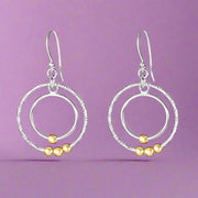 A pair of silver earrings with gold accents in a circular link design, hanging from fish hook closures.