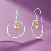 A pair of sterling silver hoop earrings with gold hearts dangling from the hoops.