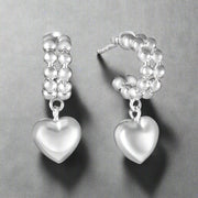 A pair of sterling silver hoop earrings with heart-shaped embellishments and pearl-like beads.