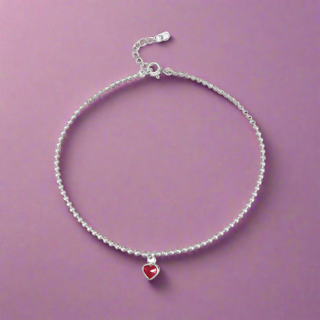 Silver anklet with a red heart charm on a white background