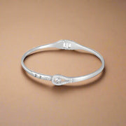 A flexible sterling silver bracelet with a heart-shaped charm and small white stones set in a band.