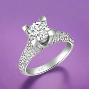 A sterling silver solitaire ring with a central cubic zirconia stone surrounded by smaller clear stones, featuring a classic six-prong setting.