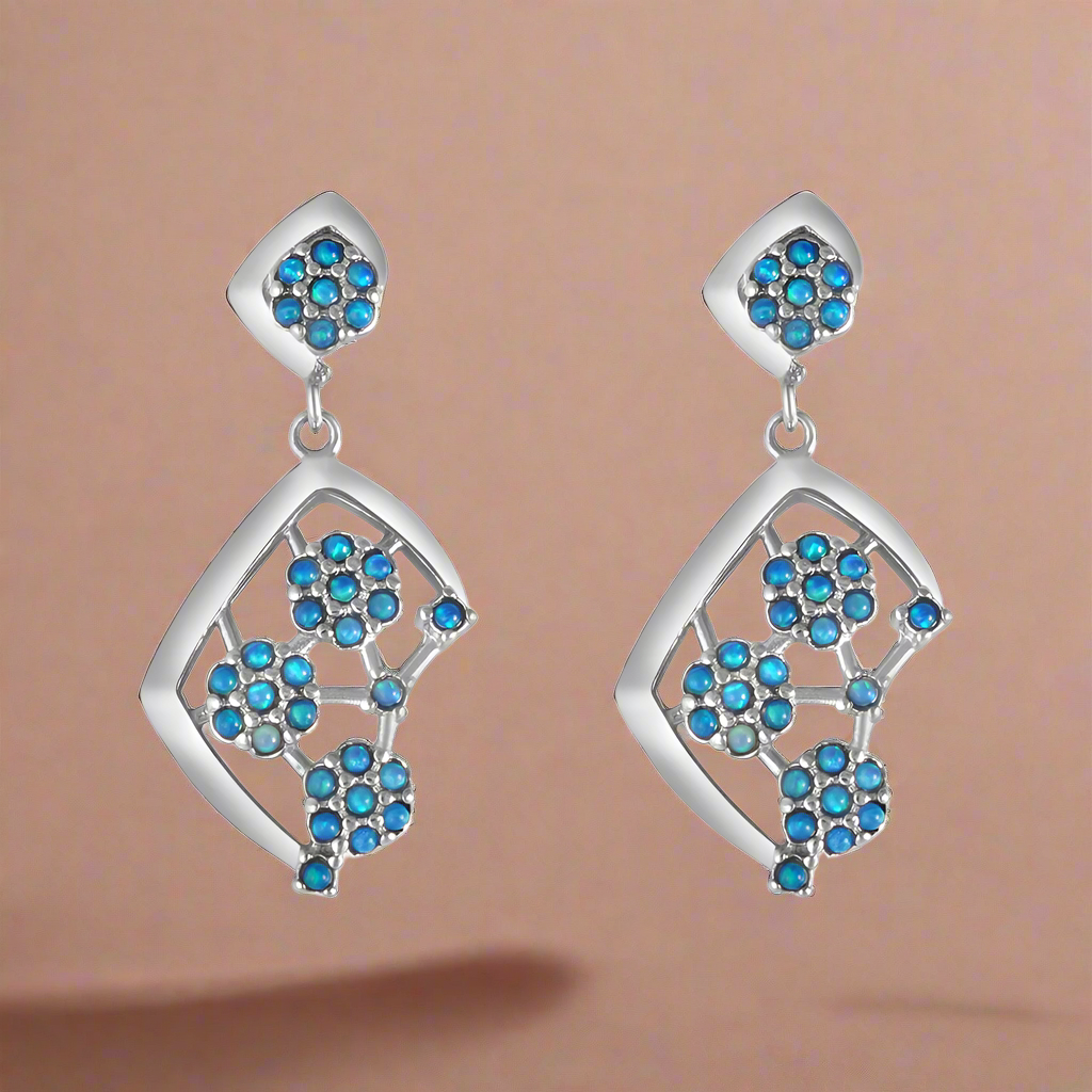 A pair of sterling silver earrings with blue firoza stones set in them, designed in a V-shape with a flowing pattern.