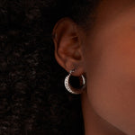 Load image into Gallery viewer, Silver hoop earring worn by a person with a dark background
