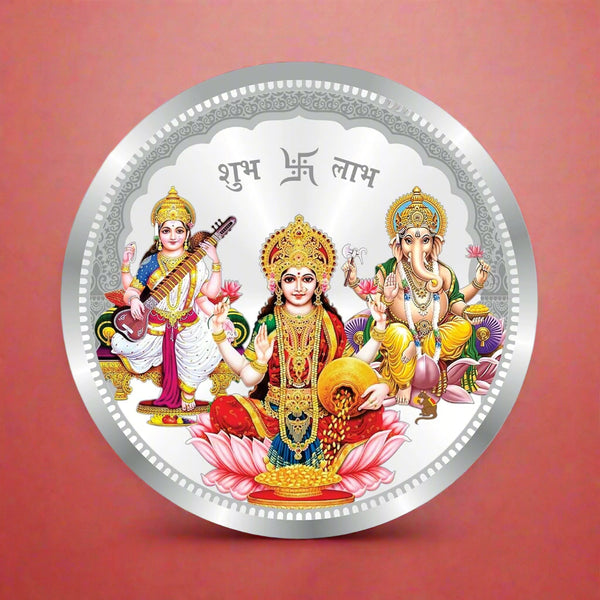 A silver coin with a circular design featuring Laxmi, Ganesh, and Saraswati, three Hindu deities, seated on a lotus with a floral background.