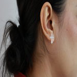 Load image into Gallery viewer, Close-up of an ear wearing a silver cross earring with hair tied back.
